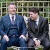 Two men in suits laughing on garden bench.