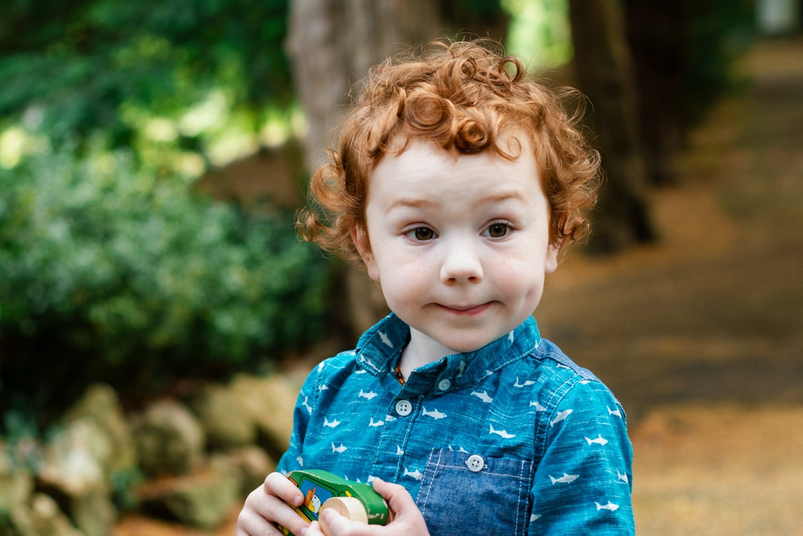 Child with curly hair holding toy outdoors