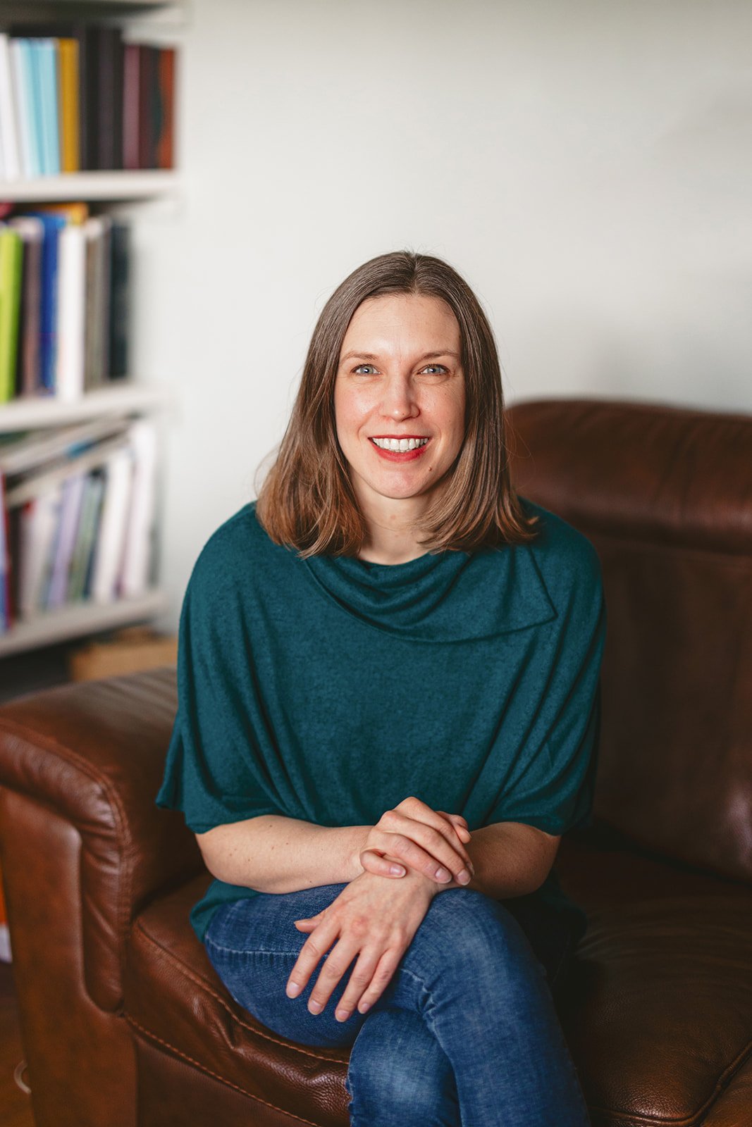 Woman smiling on leather couch, bookshelf background.