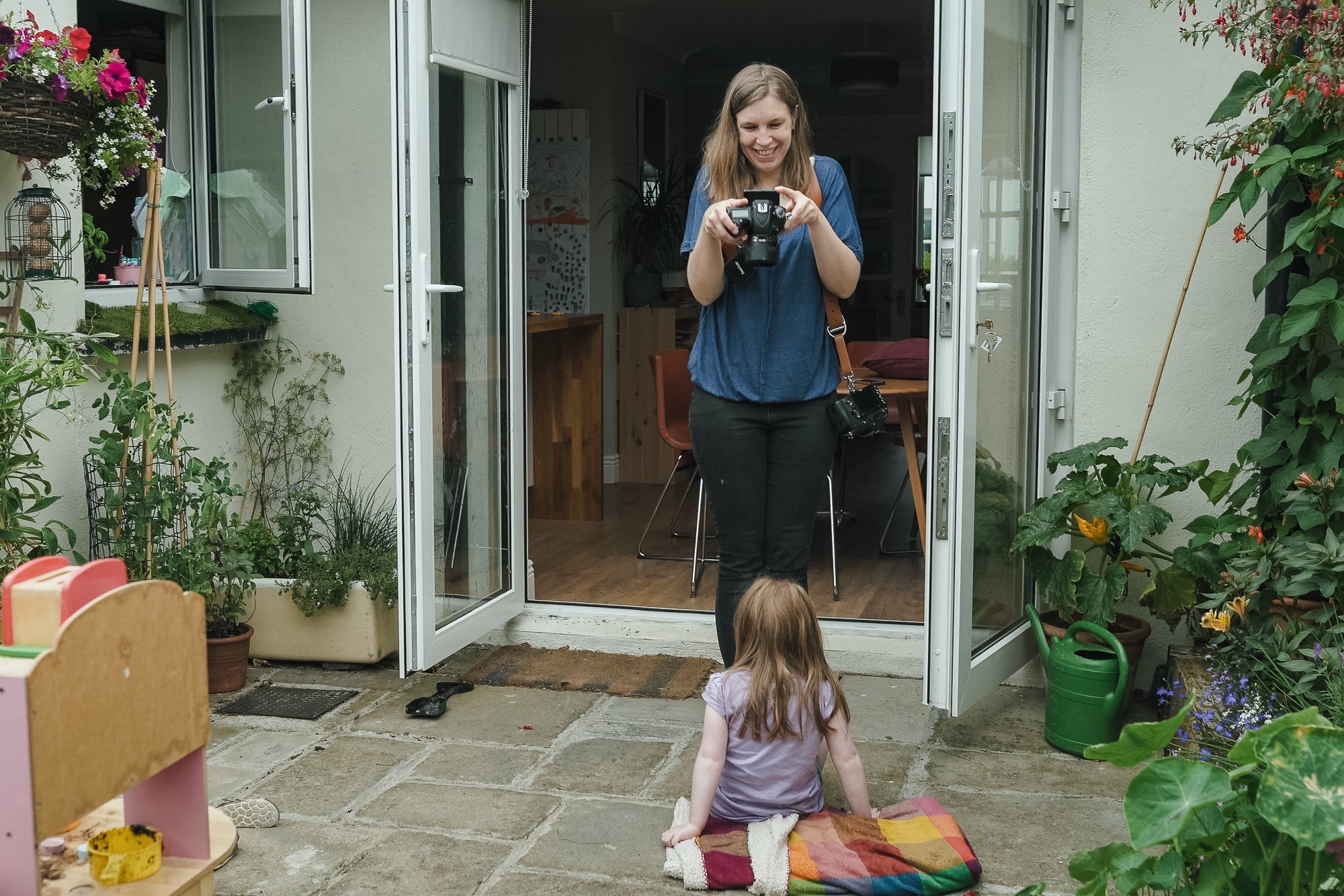 Woman photographing child in a garden patio.