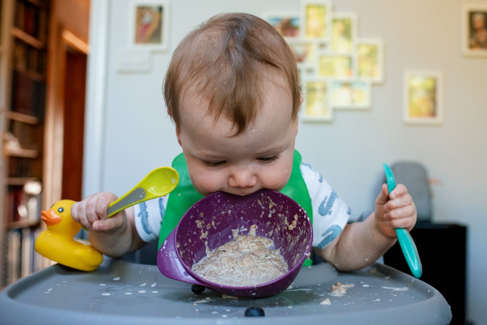 Baby eating with spoons, messy high chair.