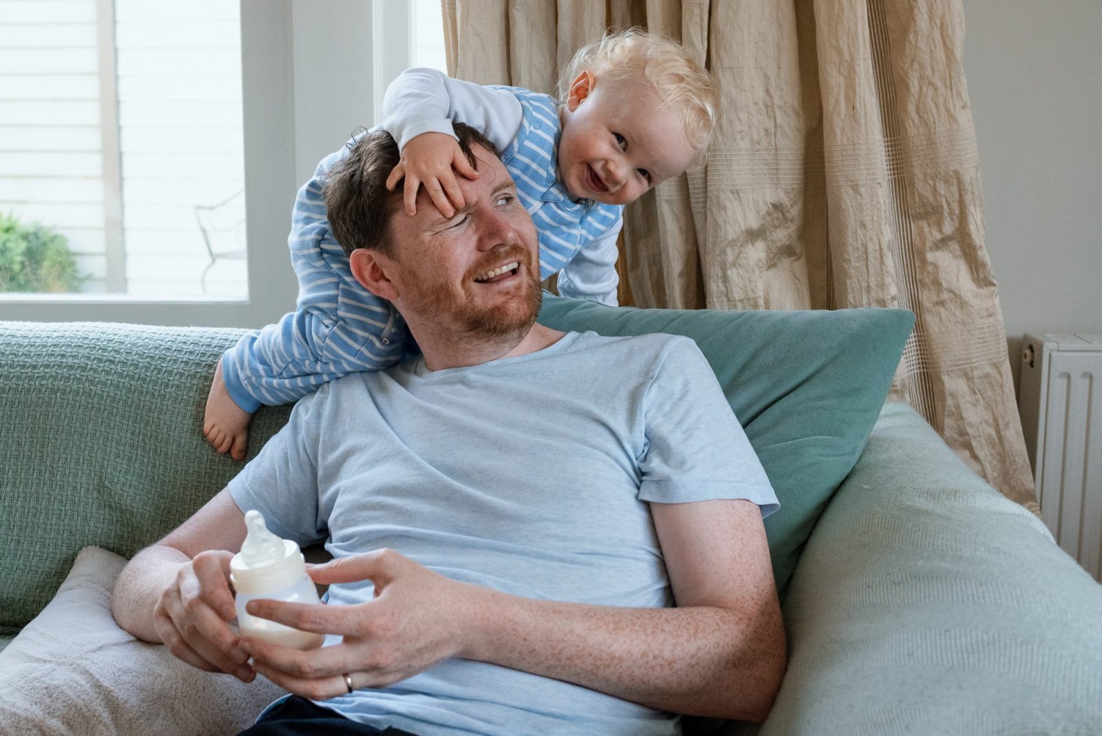 Father and toddler enjoying playful moment on sofa.