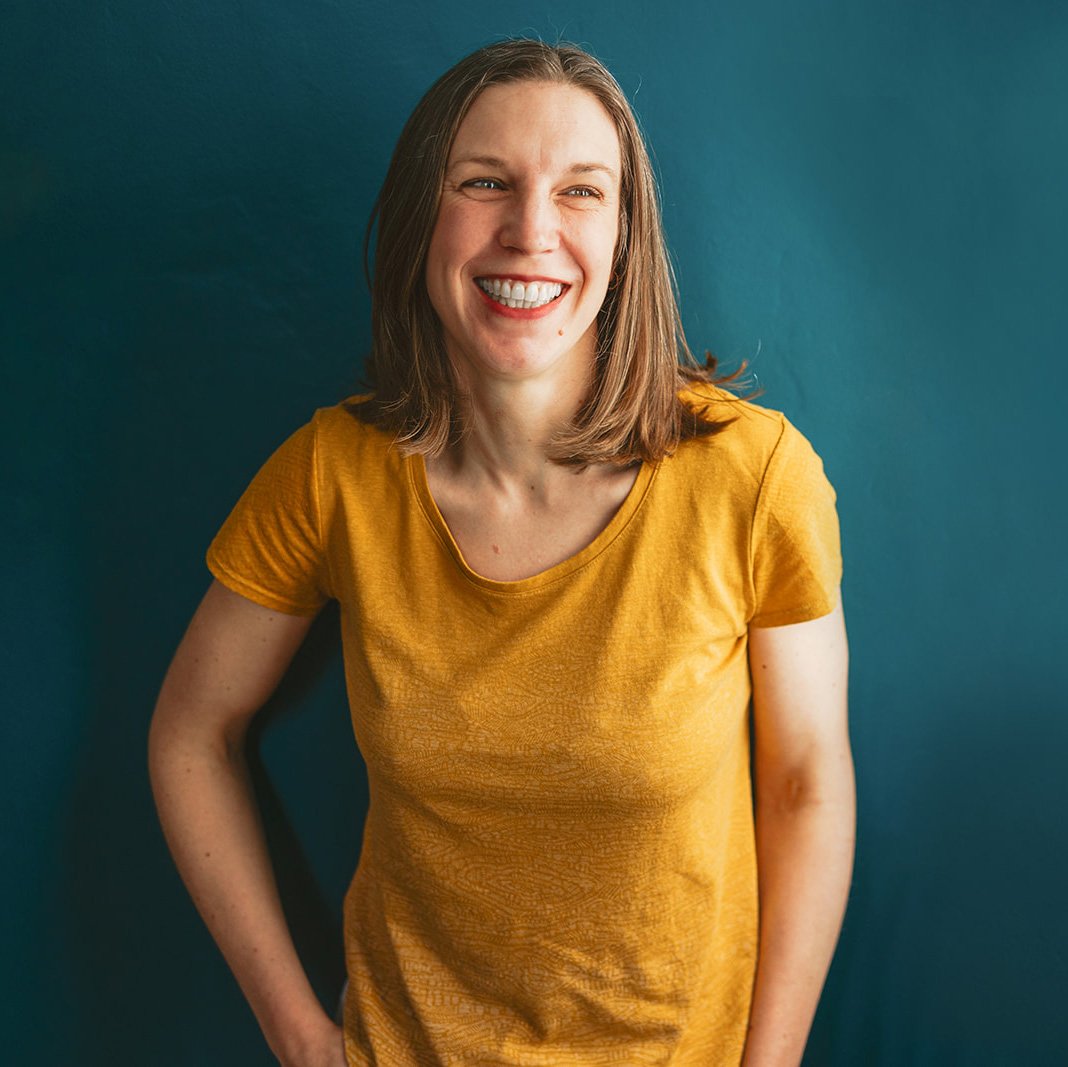Woman smiling in yellow top against blue background.