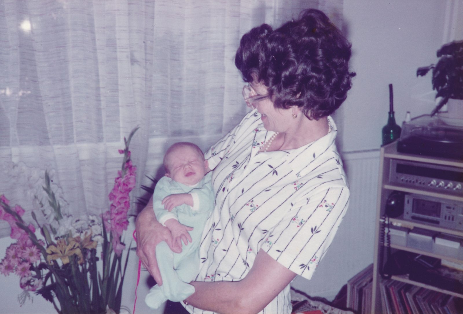 Woman holding a baby indoors near flowers.